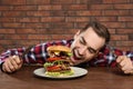 Young hungry man with cutlery eating huge burger