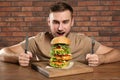 Young hungry man with cutlery eating huge burger