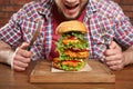 Young hungry man with cutlery and tasty huge burger