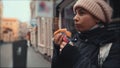 Young hungry woman traveller eats vegan meatless fast food on street at blurred European city background