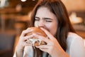 Young hungry woman in white stylish blouse biting with appetite fresh meat burger during lunch in trendy resturant eating outside Royalty Free Stock Photo