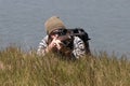 Young hunter with rifle lies on river shore