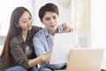 Young husband and wife holding paperwork and using laptop at home