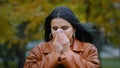 Young ill hispanic woman standing outdoors sneezing into handkerchief wiping nose feeling unwell illness seasonal cold Royalty Free Stock Photo