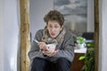 Young ill man sitting in his home with a cup of tea and a thermometer in his hands Royalty Free Stock Photo