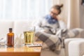 Young ill woman lying under blanket in a bed with seasonal illnes drinking hot tea with honey and lemon. She takes pills and cough