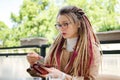 Young independent woman in eyeglasses, casual nude trench with long dreadlocks pays for her coffee in outdoor cafe