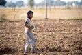 Young indian boy carrying a plastic bottle of water to father working in the field sitting on gunny bag, sacks of wheat