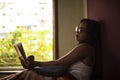 Young Indian brunette woman in white sleeping wear reading book on a bed Royalty Free Stock Photo