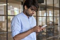 Young Indian business man using cellphone apps standing in office. Royalty Free Stock Photo