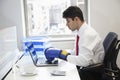 Young Indian businessman wearing boxing gloves while using laptop at office desk Royalty Free Stock Photo