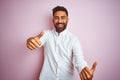 Young indian businessman wearing elegant shirt standing over isolated pink background approving doing positive gesture with hand, Royalty Free Stock Photo