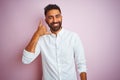 Young indian businessman wearing elegant shirt standing over isolated pink background smiling doing phone gesture with hand and Royalty Free Stock Photo