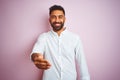 Young indian businessman wearing elegant shirt standing over isolated pink background smiling friendly offering handshake as Royalty Free Stock Photo