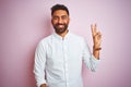 Young indian businessman wearing elegant shirt standing over isolated pink background smiling with happy face winking at the Royalty Free Stock Photo