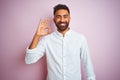 Young indian businessman wearing elegant shirt standing over isolated pink background smiling positive doing ok sign with hand and Royalty Free Stock Photo