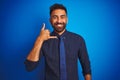 Young indian businessman wearing elegant shirt and tie standing over isolated blue background smiling doing phone gesture with Royalty Free Stock Photo