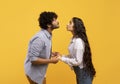 Young indian couple reaching each other with lips, ready to kiss over yellow background, side view
