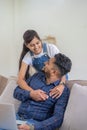 Young indian couple using laptop while sitting on couch and floor. Happy smiling indian woman embrace from behind her Royalty Free Stock Photo