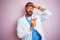 Young indian doctor man holding paper heart standing over isolated pink background stressed with hand on head, shocked with shame Royalty Free Stock Photo