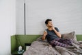 Young indian dreaming man sitting on the bed with phone