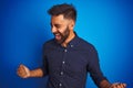 Young indian elegant man wearing shirt standing over isolated blue background very happy and excited doing winner gesture with Royalty Free Stock Photo