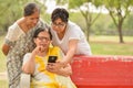 A young Indian girl with mother and mother in law - senior graceful women gossiping and smiling at the mobile phone screen while Royalty Free Stock Photo