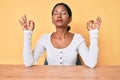 Young indian girl wearing casual clothes sitting on the table relax and smiling with eyes closed doing meditation gesture with Royalty Free Stock Photo