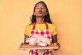 Young indian girl wearing cook apron and holding chicken looking at the camera blowing a kiss being lovely and sexy