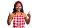 Young indian girl wearing professional baker apron success sign doing positive gesture with hand, thumbs up smiling and happy Royalty Free Stock Photo