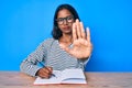 Young indian girl writing notebook sitting on the table with open hand doing stop sign with serious and confident expression, Royalty Free Stock Photo