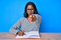 Young indian girl writing notebook sitting on the table pointing with finger to the camera and to you, confident gesture looking Royalty Free Stock Photo