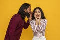 Young indian guy sharing secret with his girlfriend, yellow background Royalty Free Stock Photo