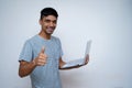 Young indian handsome boy showing thumbs up and smiling while looking into the camera, holding laptop in his other hand Royalty Free Stock Photo