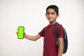 Young Indian kid holding a phone in his hand with a green screen, school bag in his back and wearing red t-shirt standing on white Royalty Free Stock Photo