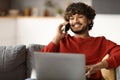 Young Indian Male Freelancer Using Laptop And Talking On Cellphone At Home Royalty Free Stock Photo