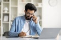 Young Indian Male Talking On Cellphone And Taking Notes To Notepad Royalty Free Stock Photo