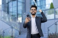 A young Indian man in a business suit and glasses is standing outside an office building, holding a mobile phone Royalty Free Stock Photo