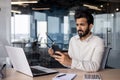 Young Indian man businessman working in office, worriedly holding glasses in hand and looking at mobile phone Royalty Free Stock Photo