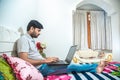 Young indian man busy working on his computer doing office work while relaxing on bed in bedroom, freelancer working from home. Royalty Free Stock Photo