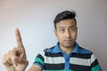 A young indian man expressing a doubtful and concerned face indicating number one with finger isolated in white background with