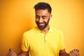 Young indian man listening to music using earphones standing over isolated yellow background very happy and excited doing winner Royalty Free Stock Photo