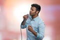 Young indian man performing lyric song on abstract pink bokeh background.