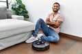 Young indian man sitting at home by vacuum robot happy face smiling with crossed arms looking at the camera