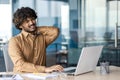 A young Indian man is suffering from severe neck pain. Tired man sits at the desk in the office and massages his hand Royalty Free Stock Photo