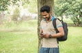 Young indian man using smartphone app in university campis - Happy asian guy having fun watching videos on mobile cell phone - Royalty Free Stock Photo