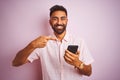 Young indian man using smartphone standing over isolated pink background very happy pointing with hand and finger Royalty Free Stock Photo