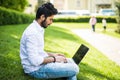 Young indian man using and typing laptop computer in summer grass in the street Royalty Free Stock Photo