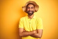 Young indian man on vacation wearing summer hat standing over isolated yellow background happy face smiling with crossed arms Royalty Free Stock Photo