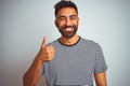 Young indian man wearing black striped t-shirt standing over isolated white background doing happy thumbs up gesture with hand Royalty Free Stock Photo